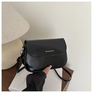 Detail of a black oil-wax leather crossbody bag on a wooden table with books