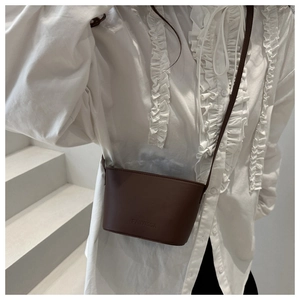 Gros plan d'un sac seau en cuir marron avec logo embossé sur un fond minimaliste blanc
