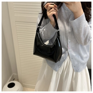 Glossy black patent leather shoulder bag detail with silver zipper on model