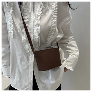Détail d'un mini sac seau en cuir marron avec logo embossé et fine bandoulière réglable