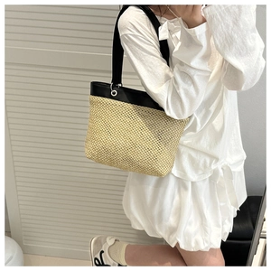 Model showing a hand-woven straw tote bag with black leather straps on white background