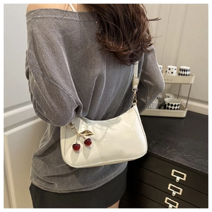 Detail of white patent leather underarm bag with cute 3D red cherry charm attachment