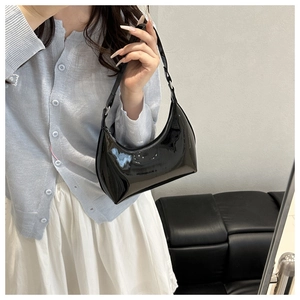 Glossy black patent leather hobo bag with adjustable strap worn on the shoulder
