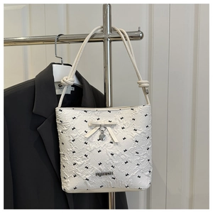 Close-up of white textured bucket bag with black bow print and metal heart charm