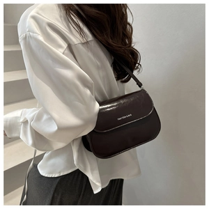 Deep coffee brown leather shoulder bag with silver logo detail worn on a model