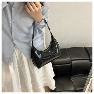 Glossy black patent leather hobo bag styled with a blue cardigan and white skirt