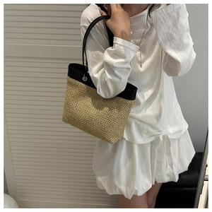 Model wearing a hand-woven straw tote bag with black leather straps for beach vacation