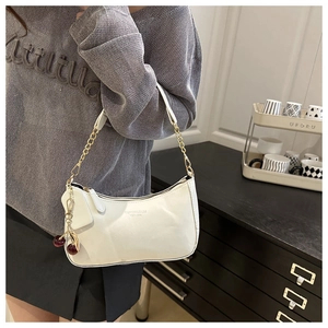 Close-up of a white hobo bag featuring a cherry charm and gold chain strap detail