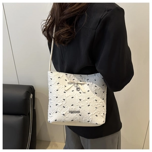 Detail of white pleated bucket bag with black bow embroidery and heart charm pendant