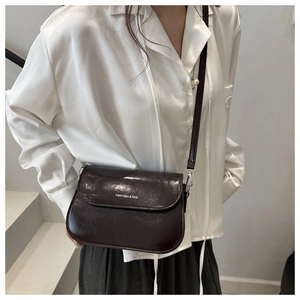Detail of dark brown glossy leather saddle bag with brand logo and slim shoulder strap