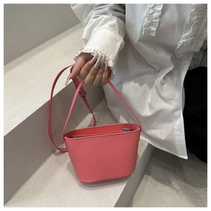 Gros plan du sac seau en cuir rose avec logo et bandoulière réglable sur l'épaule