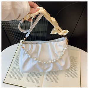 Detail of white pleated cloud bag with pearl chain and silk-wrapped handle on a book