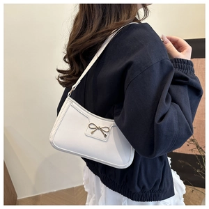 Dettaglio borsa a tracolla in pelle bianca con fiocco dorato su maglione blu