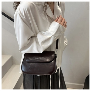 Deep brown crossbody bag with silver logo detail worn by a model on stairs