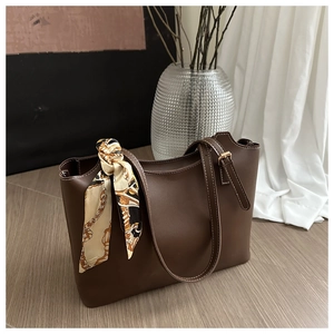 Detail of a brown tote bag featuring a chain pattern silk scarf and white stitching detail