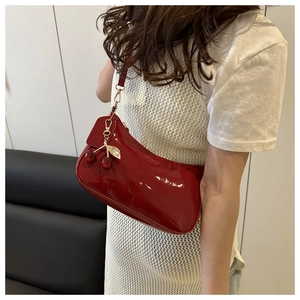 Detail of red patent leather crescent bag with a decorative metal cherry pendant