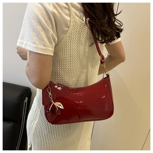 Detail of red patent leather crescent bag with golden cherry charm and fashion logo