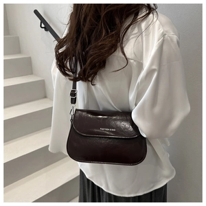 Detail of a dark brown glossy crossbody bag featuring a white logo and adjustable strap