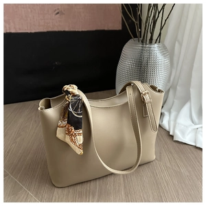 Close-up of beige bucket bag with decorative silk scarf on smooth wood floor
