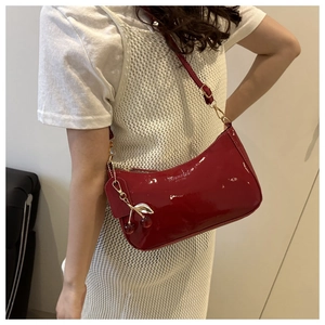 Detail of red patent leather underarm bag with cherry charm and glossy finish