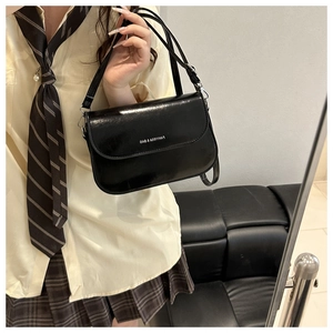Close-up of a black glossy PU leather saddle bag held by a model in a school uniform