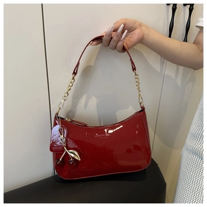 Detail of red patent leather underarm bag featuring a golden chain and cherry charm