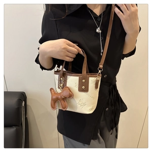 Detail der cremefarbenen Mini-Beuteltasche mit Schmetterlingsprägung und Hundeanhänger