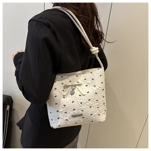 Detail of white jacquard bucket bag with black bows, metal heart pendant and knotted strap