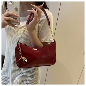 Detail of dark red patent leather hobo bag with gold chain strap and cherry charm