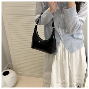 Polished black patent leather hobo bag shown on shoulder for proportion and style