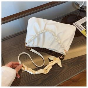 Detail of white pleated cloud bag with pearl handle and printed silk scarf on a desk