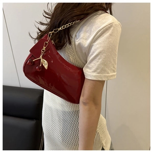 Detail of red patent leather baguette bag with metal chain and cherry charm on model