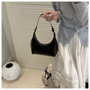 Detail of glossy black patent leather crescent bag with silver zipper and sleek finish