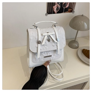Detail of white leather bag featuring a bow, heart pendant and metal Fashion logo