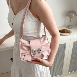 Pink bow shoulder bag with silver metal buckle in a cozy lifestyle indoor setting