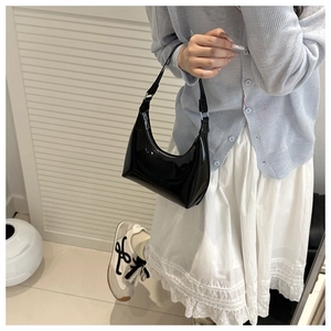 Detail of a black patent leather crescent hobo bag with sleek glossy finish on model