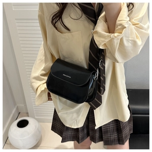 Detail of minimalist black crossbody saddle bag on a model in college style outfit