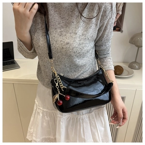 Detail of black patent leather shoulder bag with red cherry pendant and gold chain strap