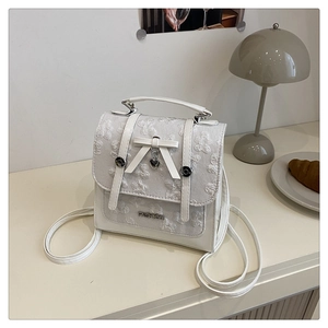 Detail of white lace mini backpack featuring floral embroidery and heart pendant