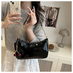 Detail of black patent leather underarm bag with gold chain and red cherry charm