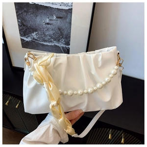 Detail of white pleated cloud bag featuring pearl handle chain and yellow silk ribbon