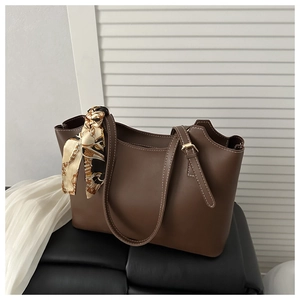 Detail of dark brown leather tote bag featuring contrast stitching and a silk scarf handle