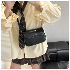 Close-up of black leather square crossbody bag with adjustable strap worn by model