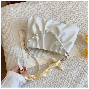Detail of white pleated cloud bag showing large pearl handle and satin ribbon decor