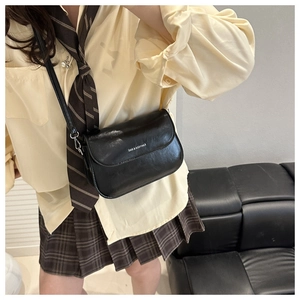 Detail of a black oily faux leather flap bag with white lettering on casual outfit