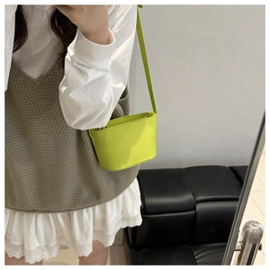 Detail of bright green mini crossbody bucket bag with embossed logo on glossy leather