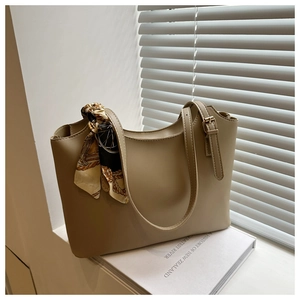 Close-up of beige tote bag featuring a decorative silk scarf and adjustable strap on a ledge