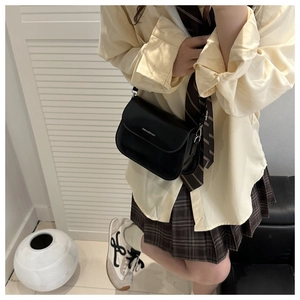 Detail of minimalist black crossbody bag with silver lettering on textured PU leather