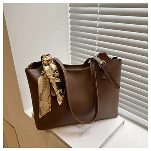 Detail of dark brown leather tote bag featuring a decorative patterned silk scarf handle