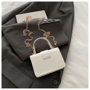 White leather mini handbag with gold chain strap on a dark gray blazer background